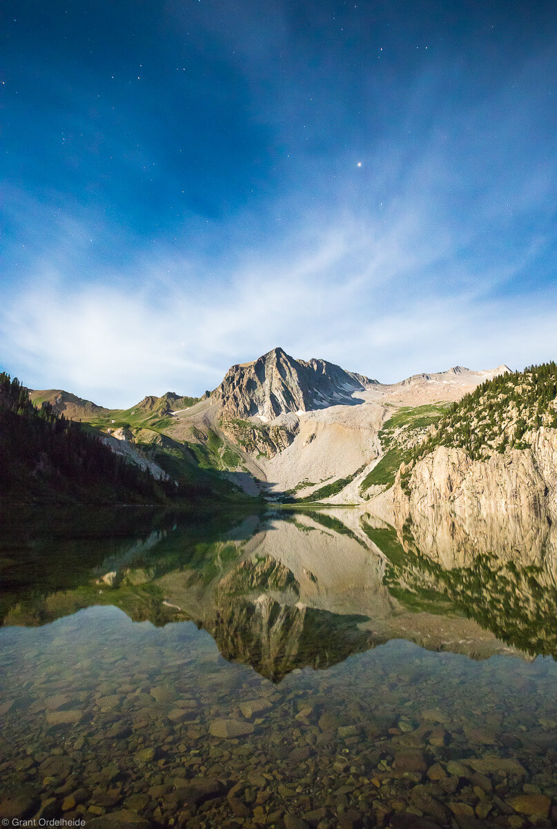 Snomass peak reflected in Snowmass lake illuminated by moonlight.