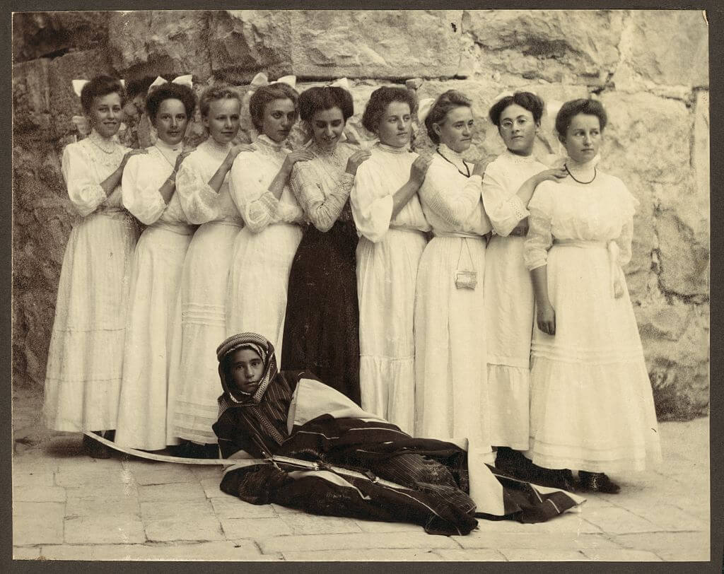 Nine girls standing over young boy holding sword